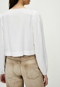 Hvid cropped bluse med puffærmer, lavet af letvægtsstof. Sammen med højhævede lys beige jeans med baglommer.