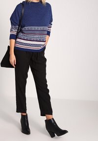 Niebieski sweter z dzianiny w białe i czerwone wzory w paski, zestawiony z czarnymi zwężającymi się spodniami i czarnymi botkami na obcasie. Czarna torebka typu tote.