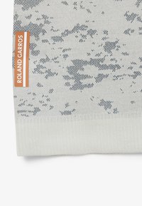 Tissu gris clair avec motif abstrait gris foncé et une étiquette orange verticale indiquée "ROLAND GARROS" sur le côté gauche.