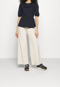 Marinblå peplum top med korte puffærmer, parret med cremefarvede bukser med vidde og sorte sneakers med hvide detaljer og en struktureret sål.