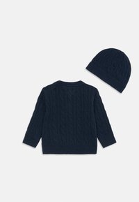 Mornarsko plavi pleteni pulover s kabelnim uzorkom i rebrastim manžetama, upareno s odgovarajućom rebrastom kapom. Mekana tekstura, klasičan dizajn.