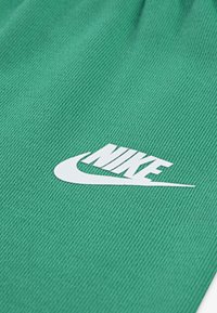 Zielony materiał o ryflowanej fakturze z białym logo Nike. Materiał wydaje się miękki i elastyczny, odpowiedni do odzieży sportowej.