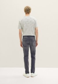 Maglietta grigia a maniche corte con una trama mélange, abbinata a jeans slim-fit grigio scuro e sneakers bianche, fotografata da dietro.