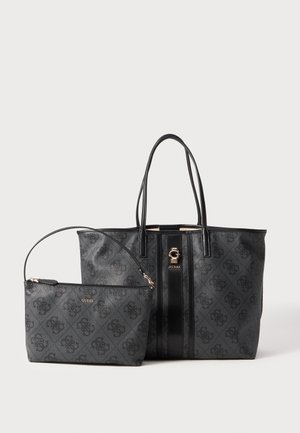 Black textured tote bag with gold hardware and striped detail, paired with a smaller black zip pouch. Both feature the "GUESS" logo.