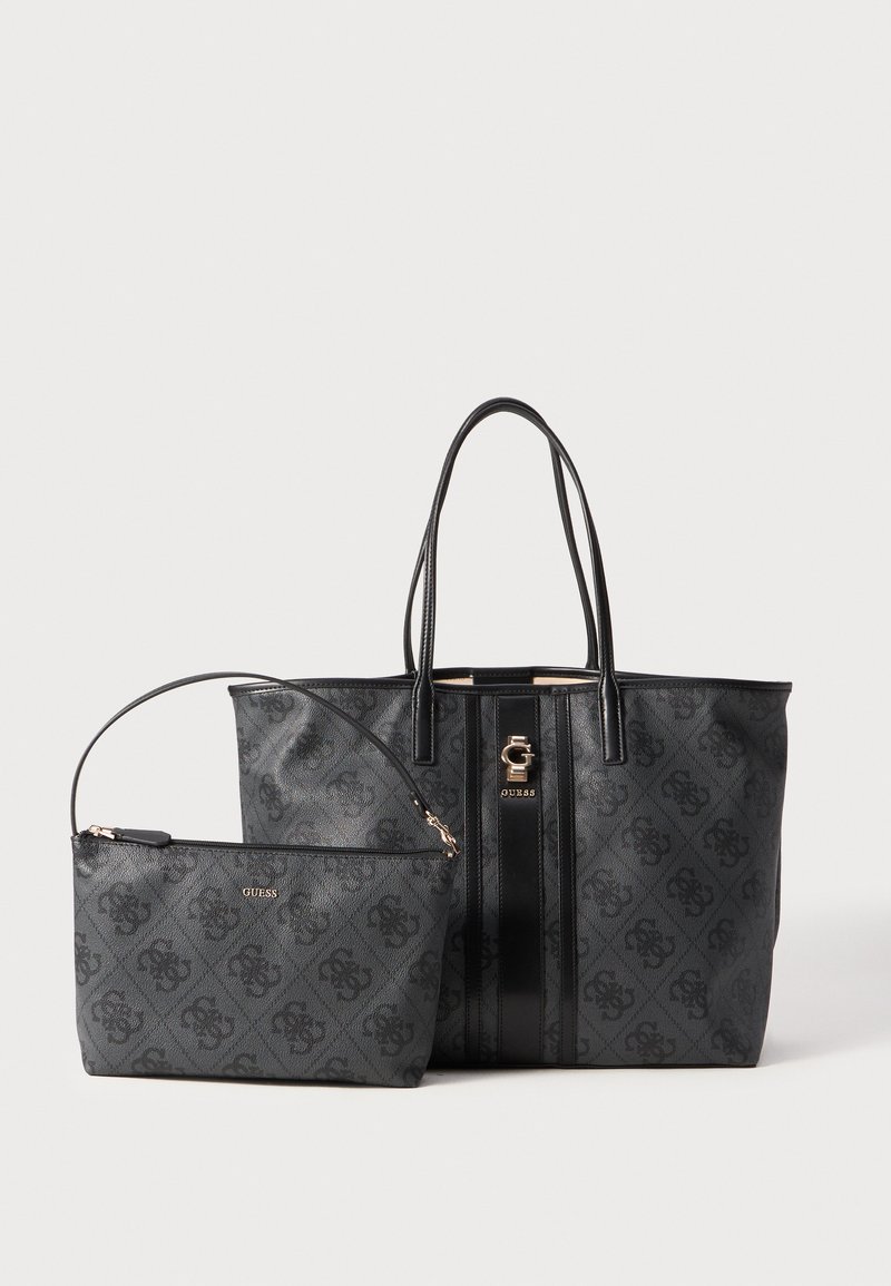 Zwarte gestructureerde tote bag met gouden hardware en gestreept detail, gecombineerd met een kleinere zwarte ritsportemonnee. Beide zijn voorzien van het 'GUESS' logo.