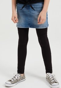 Denim mini krilo v svetlo modri barvi, kombinirano s črnimi legicami in supergami z leopardjim vzorcem. Material se zdi mehak, gladek zaključek brez vzorcev.