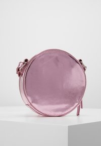 Bolso redondo de imitación de cuero metálico rosa, con una textura suave, cierre de cremallera y una correa desmontable. Diseño minimalista sin adornos visibles.