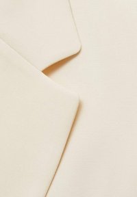 Tissu de couleur crème avec une texture lisse et un motif finement tissé. Présente des sections superposées et des bords angulaires nets.