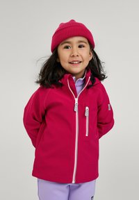 Veste softshell rose vif avec une fermeture éclair à l'avant, matériel gris et capuche ajustée. Associée à un haut violet et un bonnet rose assorti.