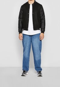 Black bomber jacket with leather sleeves, white t-shirt, loose blue jeans, and black and white sneakers. Smooth textures with no visible patterns.