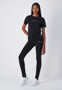 T-shirt in cotone nero e leggings con logo "Champion" in oro. I leggings hanno una vestibilità aderente; la t-shirt presenta un collo rotondo e maniche corte.