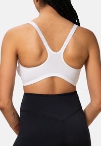 Biały sportowy stanik z wycięciem typu racerback, teksturowaną tkaniną i elastyczną opaską. Połączony z czarnymi legginsami o wysokim stanie widocznymi poniżej.