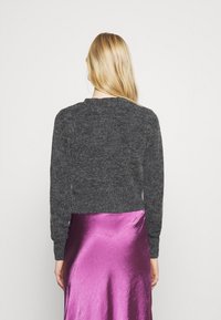 Tmavě šedý, texturovaný svetr s dlouhými rukávy, kulatým výstřihem a zkráceným střihem, v kombinaci s lesklou fuchsiovou saténovou sukní.