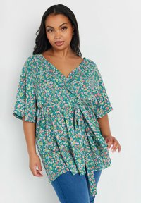 Top avvolgente floreale in teal con maniche corte a sbuffo, caratterizzato da una cintura annodata e una combinazione di piccoli fiori rosa, gialli e bianchi su un tessuto texturizzato.