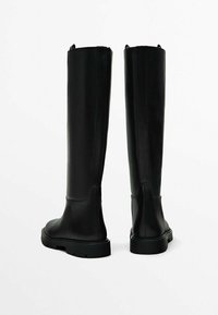 Bottes noires en cuir montant jusqu'au genou avec une texture lisse, un bout arrondi et une semelle noire épaisse. Équipées de languettes à l'arrière pour un enfilage facile.
