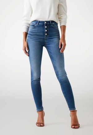 Jeans skinny din denim albastru, cu talie înaltă, cu sistem de închidere cu cinci butoane, buzunare frontale și un finisaj decolorat. Purtați cu sandale cu bretele bej.