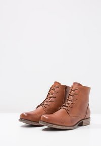 Botas de cuero marrón hasta el tobillo con puntera redonda, cordones en la parte delantera y cremallera lateral. Presentan una suela de goma marrón texturizada y costuras mínimas.