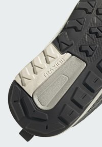 Primer plano de la suela de un zapato que muestra una banda de rodadura de goma negra y blanca con patrones triangulares y el texto "TRAXION" en el centro.