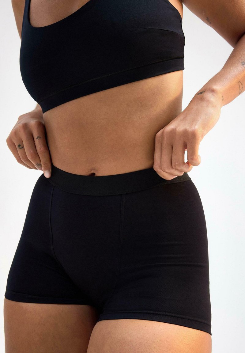 Reggiseno sportivo nero e pantaloni shorts a vita alta, realizzati in un tessuto liscio con vestibilità elasticizzata, dotati di una cintura senza cuciture e design minimalista.