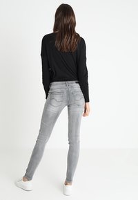 Jeans skinny grises con bolsillos traseros, que presentan un sutil acabado desgastado y una tela suave y elástica. Combinados con una camiseta de manga larga negra.