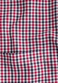 Tissu à carreaux rouge, blanc et bleu marine avec une petite poche cousue dans le coin inférieur droit.