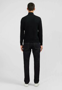 Pull noir avec un col haut, coupe ajustée. Associé à un jean bleu foncé et des baskets blanches. Texture lisse, design minimal, sans logos visibles.