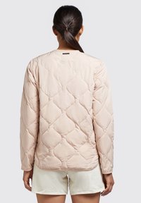 Light pink quilted jacket with a round neckline, textured diamond pattern, and long sleeves, worn over white shorts.
