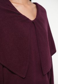 Tumepunane kootud džemper, millel on pehme, tekstureeritud kangas, V-kaelus ja kihiline krae disain. Ei ole nähtavaid riistvara osi ega aksessuaare.