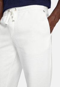 White cotton jogger pants with elastic waistband and drawstring, featuring side pockets and a smooth, textured fabric finish.