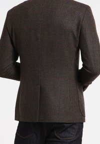 Mönstrad tweedblazer i mörkbrun herringbone med subtila blå och röda accenter. Har en skräddarsydd passform och två bakventiler.