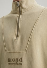 Jasno beżowy sweatshirt z kołnierzem na pół zamku, teksturowanym materiałem, wyraźnym przeszyciem i naszywką z haftem "mopd MarcOPolooDenim".