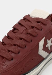 Red leather sneaker with matching laces, prominent white star logo, textured panels, and a black rubber sole. Classic low-top design.