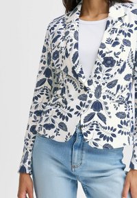 Blazer navy a fantasia floreale con design strutturato, realizzato in tessuto morbido. Presenta un rever a notched e tasche frontali, abbinato a jeans chiari.