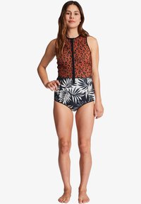 Een wetsuit met een bovenstuk met luipaardprint in bruin en een zwarte high-waisted onderkant met een wit tropisch bladenpatroon, met een ritssluiting aan de voorkant.
