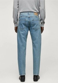 Jeans in denim azzurro chiaro con vestibilità rilassata, cinque tasche e un'etichetta in pelle sul retro. La texture è leggermente sbiadita con una finitura liscia.