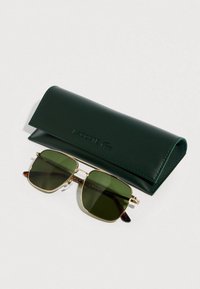 Green-tinted rectangular sunglasses with gold metal frames resting below a dark green Lacoste case on a white surface.