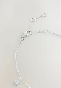 Delicate silver chain necklace with adjustable links, a lobster clasp, and a small star-shaped charm with a central gemstone.