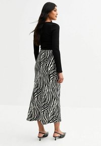 Top negro de manga larga con relieve, combinado con una falda fluida de longitud media con estampado de cebra en blanco y negro, y tacones negros con correas en el tobillo.