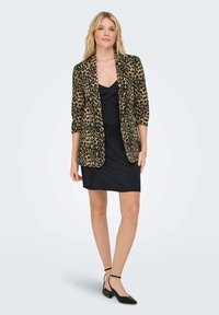 Blazer s uzorkom leoparda od mekog materijala, s dugim rukavima i otvorenim prednjim dijelom, nosi se preko crne uske haljine i crnih štikli.