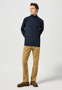 Maglione a collo alto navy in tessuto morbido, abbinato a pantaloni in velluto a coste marrone chiaro e mocassini marroni con dettagli a nappe.