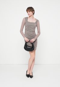 Rochie lungă, cu mâneci transparente, având un decolteu pătrat și un model în carouri în nuanțe neutre. Geantă neagră, cu o formă rotundă și o textură fină.