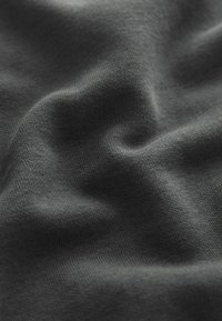Dunkelgrauer Stoff mit einer weichen Textur, der eine glatte, gleichmäßige Webart und subtile Falten aufweist, die eine wellenartige Erscheinung erzeugen.