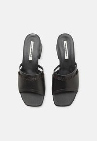 Sandales à talons noirs avec une finition lisse, présentant de larges brides et une bande de logo. Design à talon carré et semelle texturée pour une bonne adhérence.