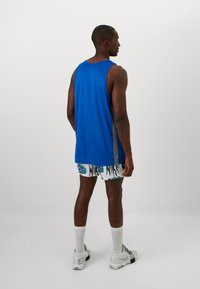 Top sportivo blu con accento grigio, abbinato a pantaloni corti bianchi con un motivo a logo Nike blu e nero. Modello che indossa sneakers.