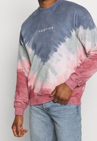 Felpa tie-dye nei toni del blu, rosa e verde. Presenta un collo rotondo e polsini a coste. Logo "KAOTIKO" centrato sul petto.