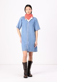 Denim shirt dress with short sleeves, front buttons, and side pockets. Paired with a red patterned scarf and brown knee-high boots.