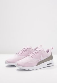 Zapatillas Nike con parte superior de malla suave en color rosa claro y detalles en gris, puntera redonda, diseño de cordones y suela de goma blanca con amortiguación de aire.