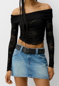 Černý top s odhalenými rameny z texturované látky, s dlouhými rukávy a vlnitým vzorem. Kombinován s modrou džínsovou minisukní a černým opaskem se cvočky.