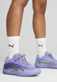 Lila Sportschuhe verfügen über ein strukturiertes Obermaterial mit grünen Akzenten, eine Schnürung und eine gemusterte Sohle. Weiße gerippte Socken runden den Look ab.