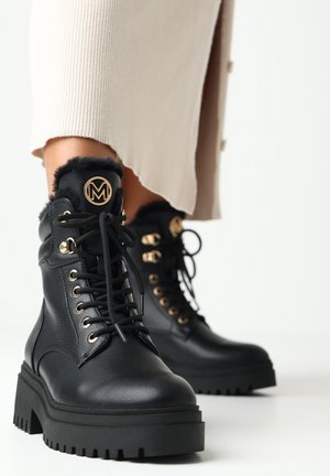 Schwarze Lederstiefeletten mit goldener Hardware, plüschigem schwarzen Pelzkragen, runder Zehenpartie und dicker, strukturierter schwarzer Gummisohle.